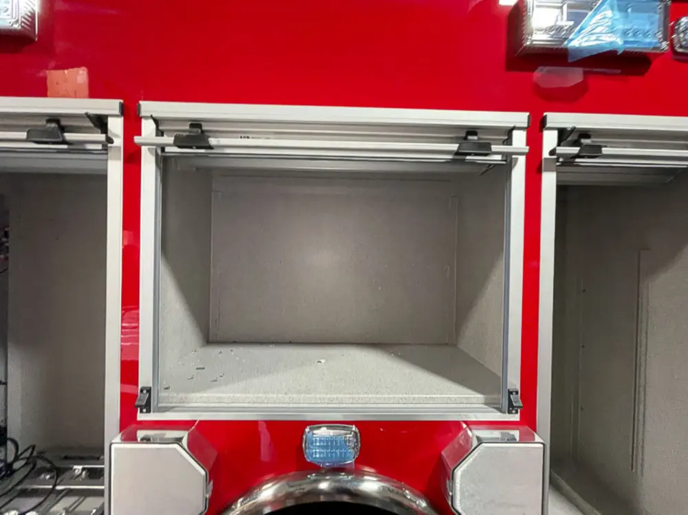 Exterior view of small fire truck showing cab, body compartments, and wheel/tire area.